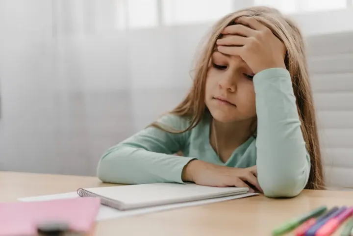 Ein Mädchen sitzt erschöpft am Schreibtisch und stützt den Kopf in die Hand