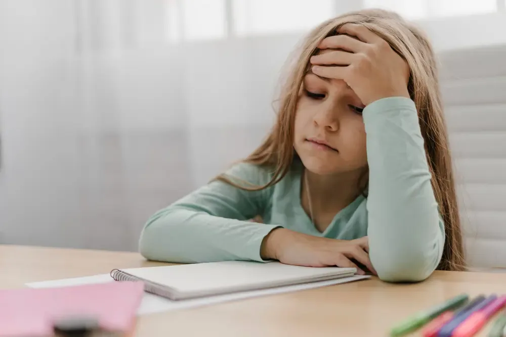 Ein Mädchen sitzt erschöpft am Schreibtisch und stützt den Kopf in die Hand
