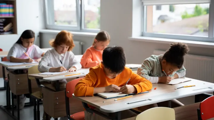 Kinder schreiben an ihren Tischen in einem Klassenzimmer